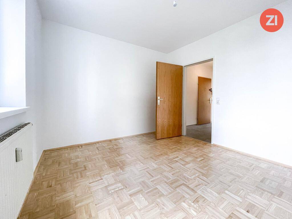 Leeres Zimmer mit Parkettboden und Holztür, bereit zur individuellen Gestaltung.