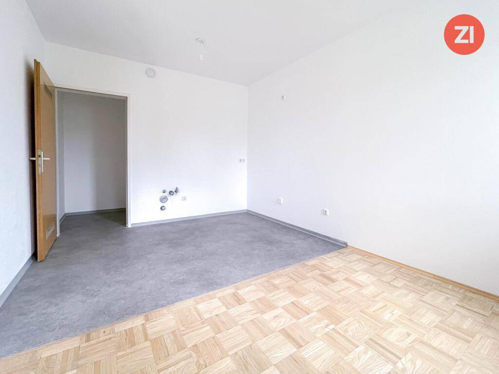 Leerer Raum mit gemischtem Bodenbelag und Zugang zu einem weiteren Zimmer.