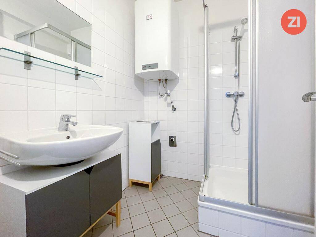 Gefliestes Badezimmer mit Dusche, Waschbecken und Warmwasserboiler.