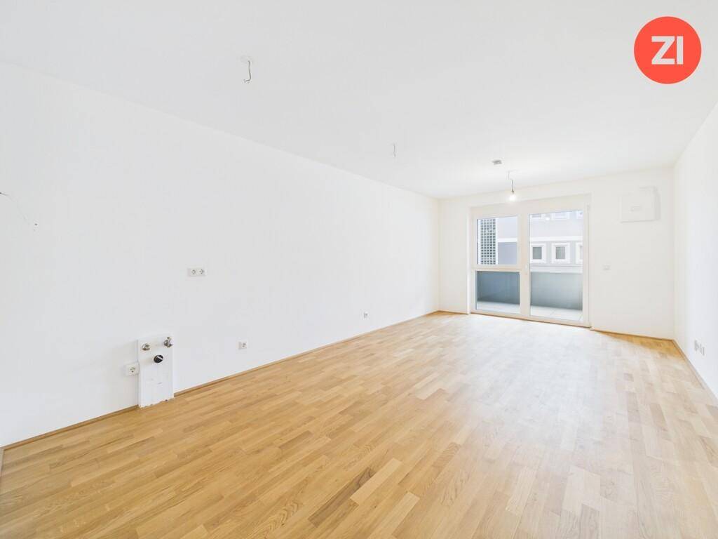 Geräumiger Raum mit Holzboden, Balkonzugang und Anschlüssen für eine Küche.