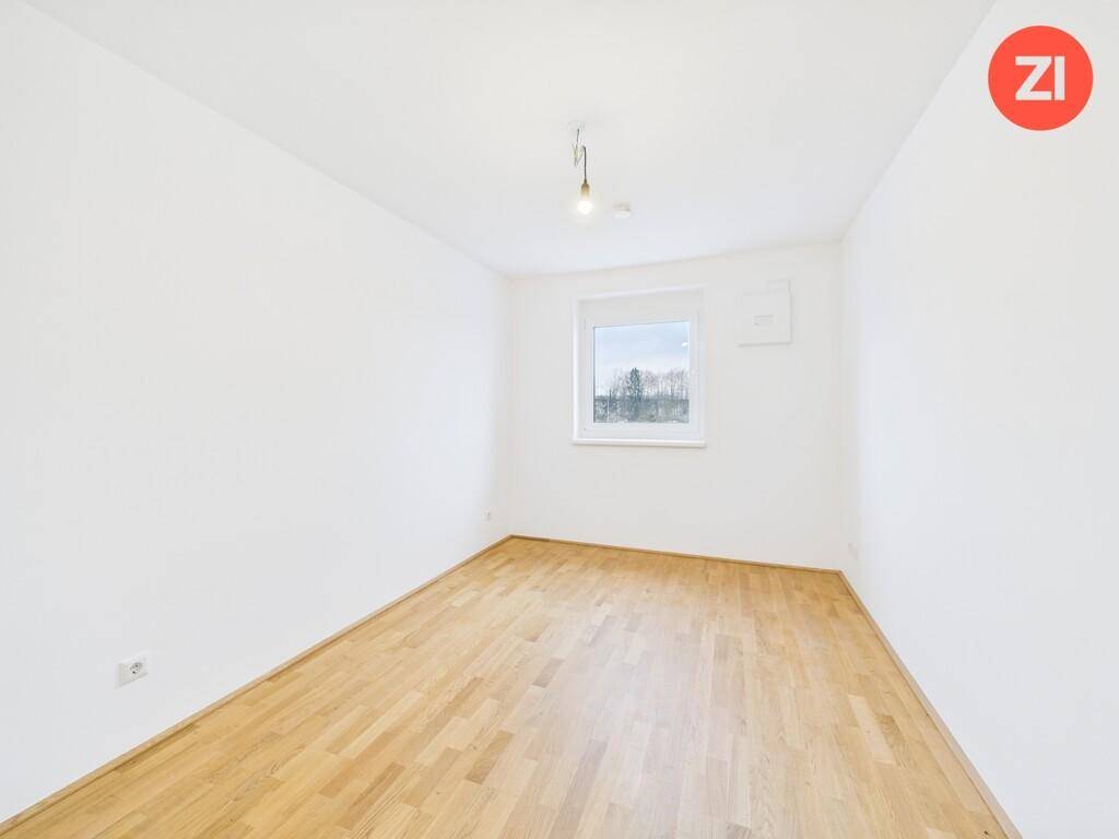 Helles Schlafzimmer mit Parkettboden und einem Fenster, das viel Tageslicht hereinlässt.