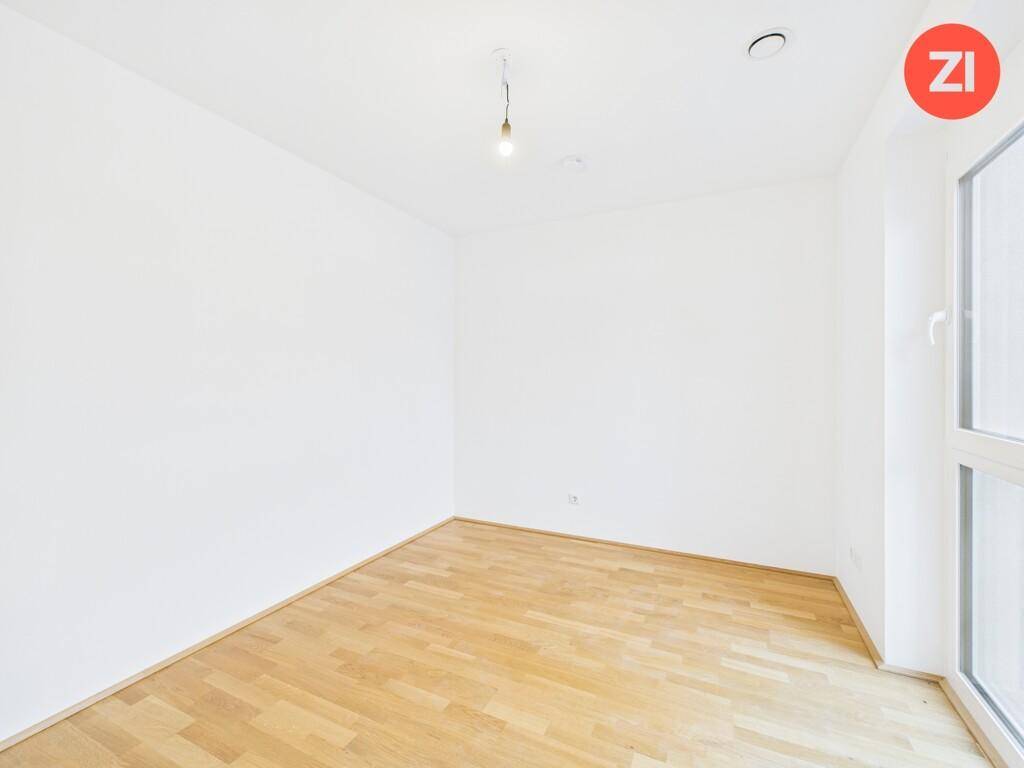 Leeres Zimmer mit hellem Parkettboden und großem Fenster, bereit zur individuellen Gestaltung.