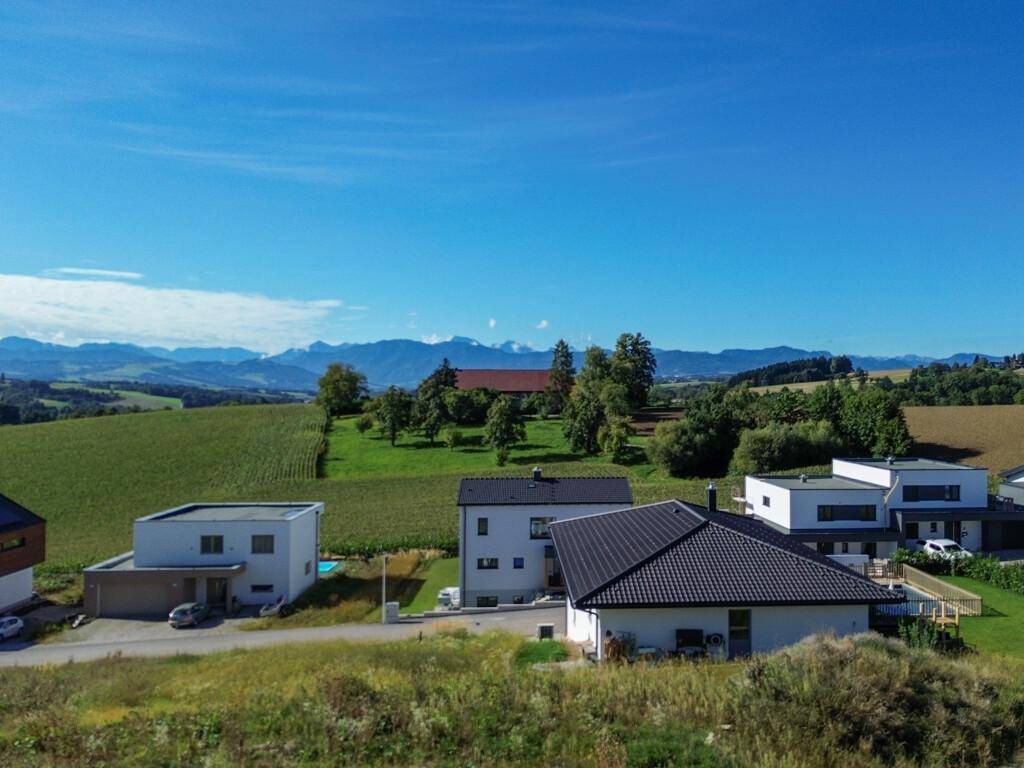 Weitläufige Luftaufnahme einer Wohnsiedlung mit grünen Feldern und beeindruckendem Bergblick im Hintergrund.