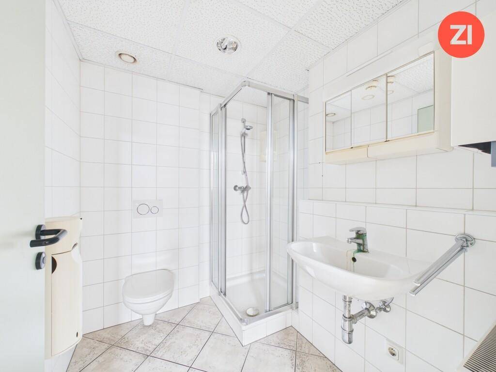 Helles Badezimmer mit Duschkabine, WC und Waschbecken, ausgestattet mit weißen Wandfliesen.