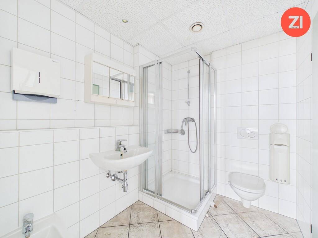 Funktionales Badezimmer mit Duschkabine, Waschbecken und WC, komplett gefliest in Weiß.