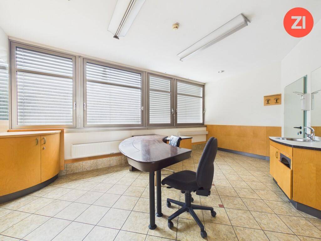 Geräumiges Büro mit großen Fenstern, Fliesenboden und einem Schreibtisch, bereit zur Nutzung.