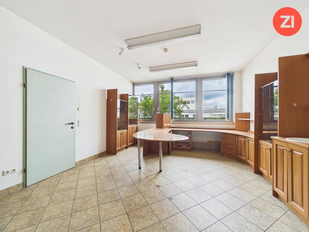 Helles Büro mit großen Fenstern, Fliesenboden und funktionalen Holzmöbeln, ideal für Arbeitsplätze.