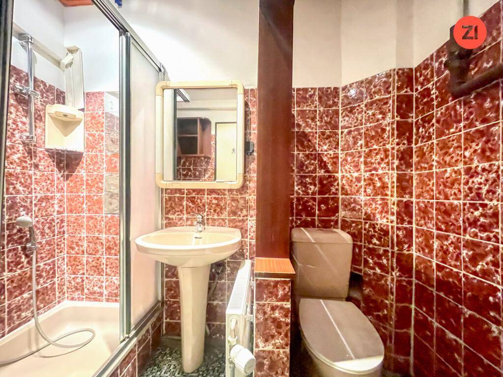 Badezimmer mit roten Fliesen, Duschkabine, Standwaschbecken und Toilette in älterem Zustand.