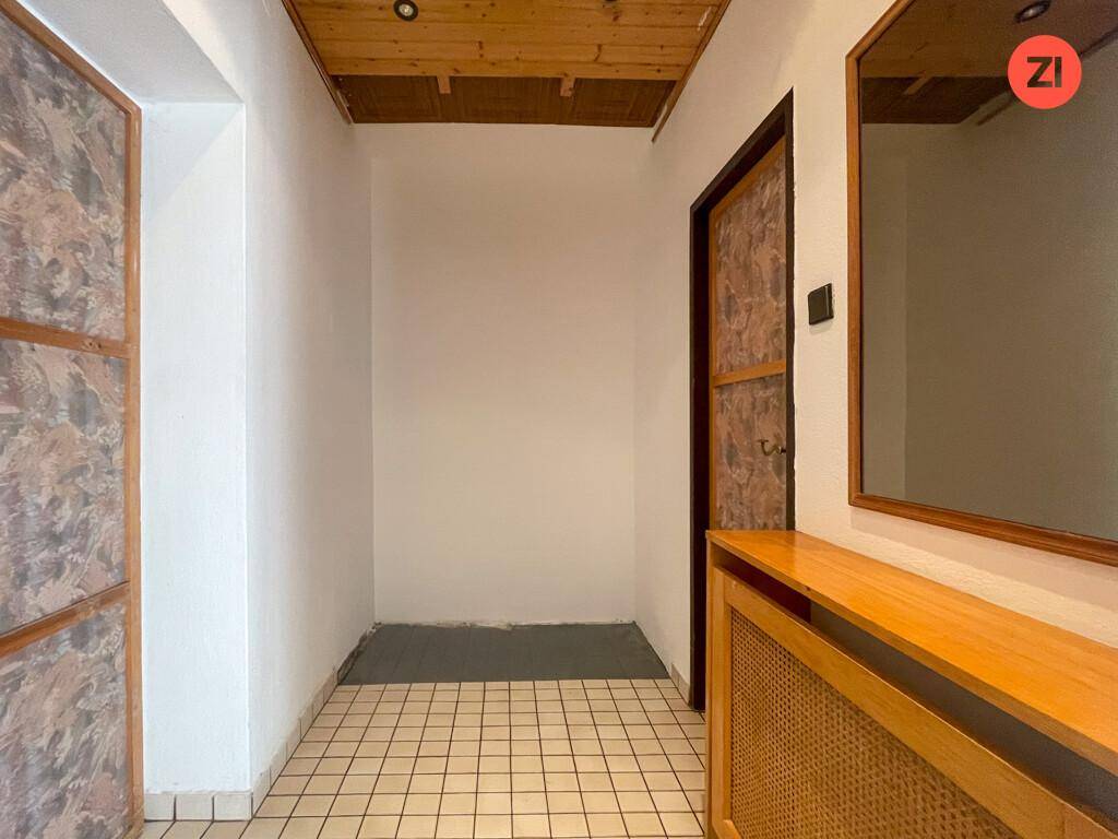 Eingangsbereich mit Fliesenboden, Holzdecke und einem Spiegel über einer Heizungsverkleidung.