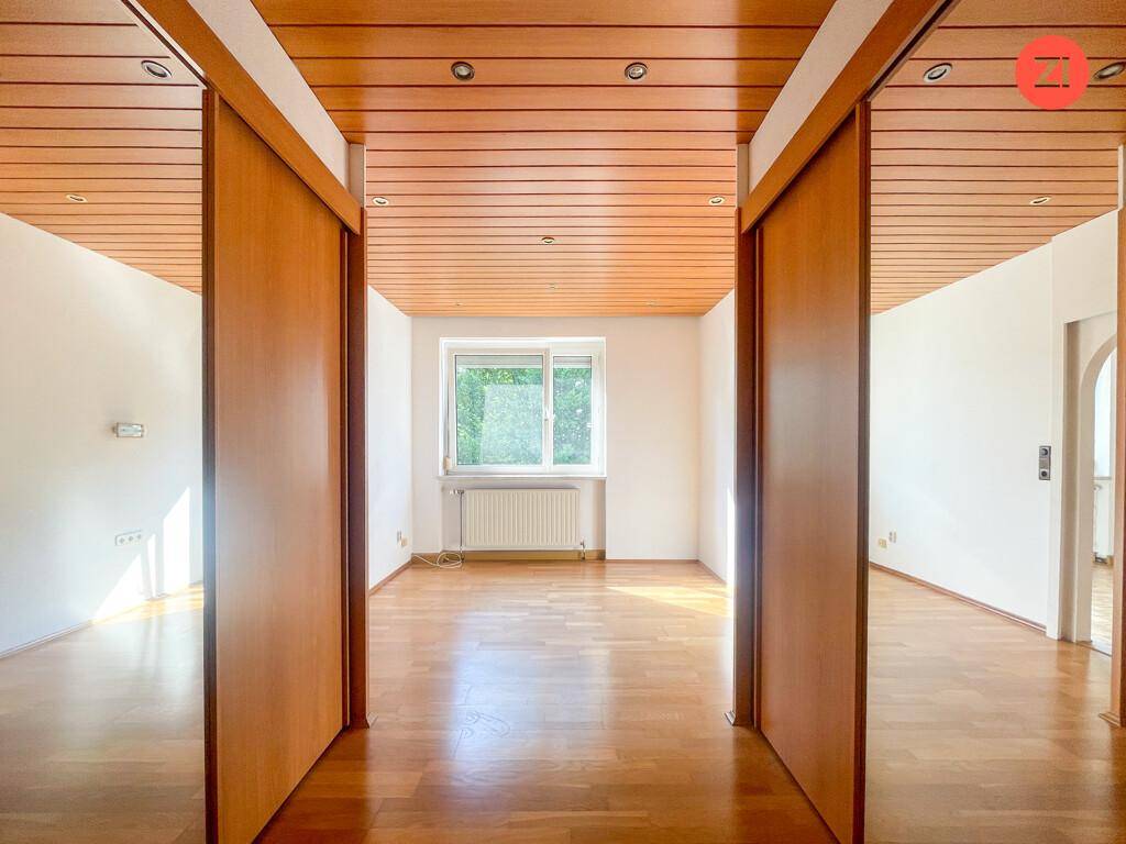 Flur mit Holzschiebetüren, Holzdecke und Parkettboden, der zu einem hellen Zimmer führt.