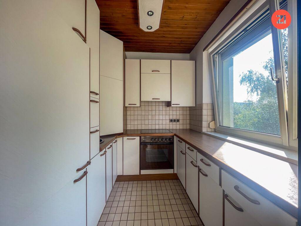 Funktionale Küche mit weißen Schränken, Holzarbeitsplatten, Fliesenboden und Holzdecke.