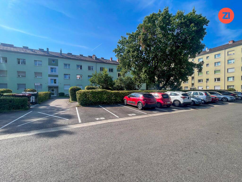 Außenparkplätze vor einem Wohngebäude mit Bäumen und Grünflächen in der Umgebung.