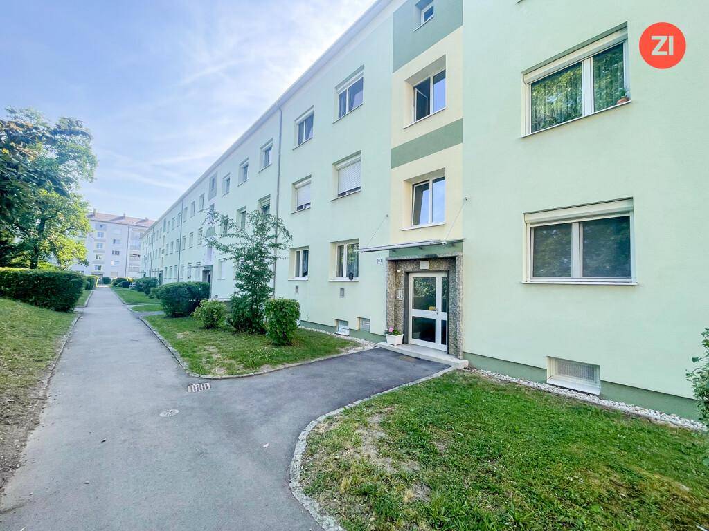 Mehrfamilienhaus mit hellgrüner Fassade, vielen Fenstern und gepflegter Außenanlage.