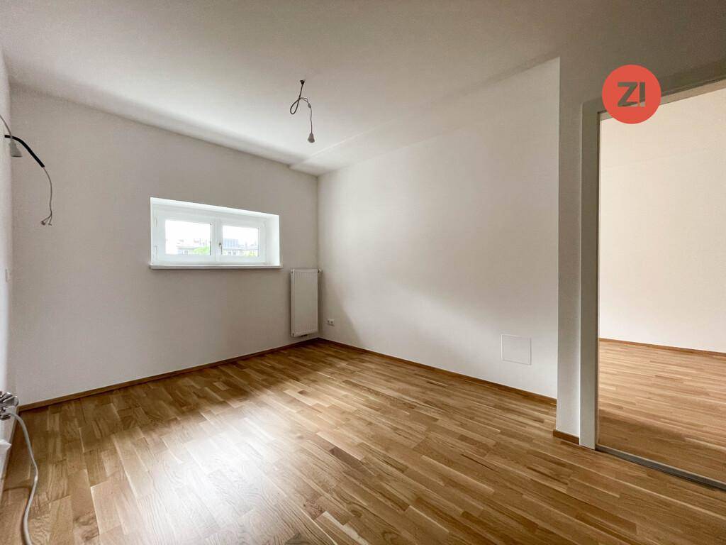 Unmöbliertes Zimmer mit Parkettboden und einem Fenster, das viel Tageslicht hereinlässt.