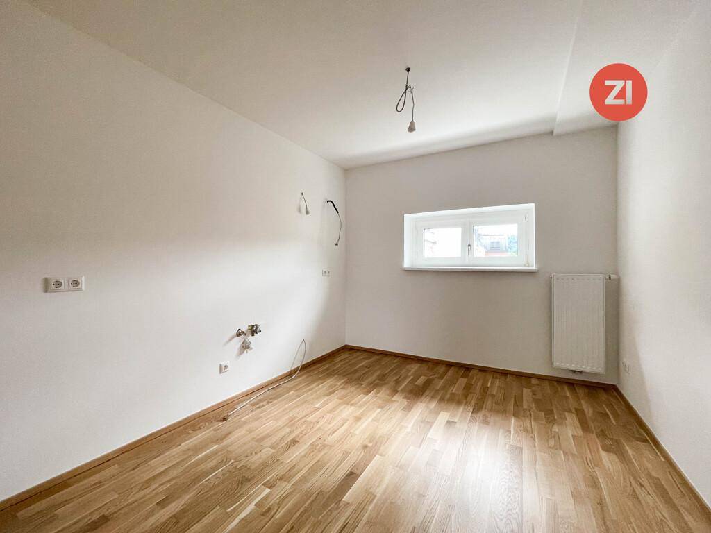 Leerer Raum mit Parkettboden und Fenster, vorbereitet für die Installation einer Küche oder als weiteres Zimmer.