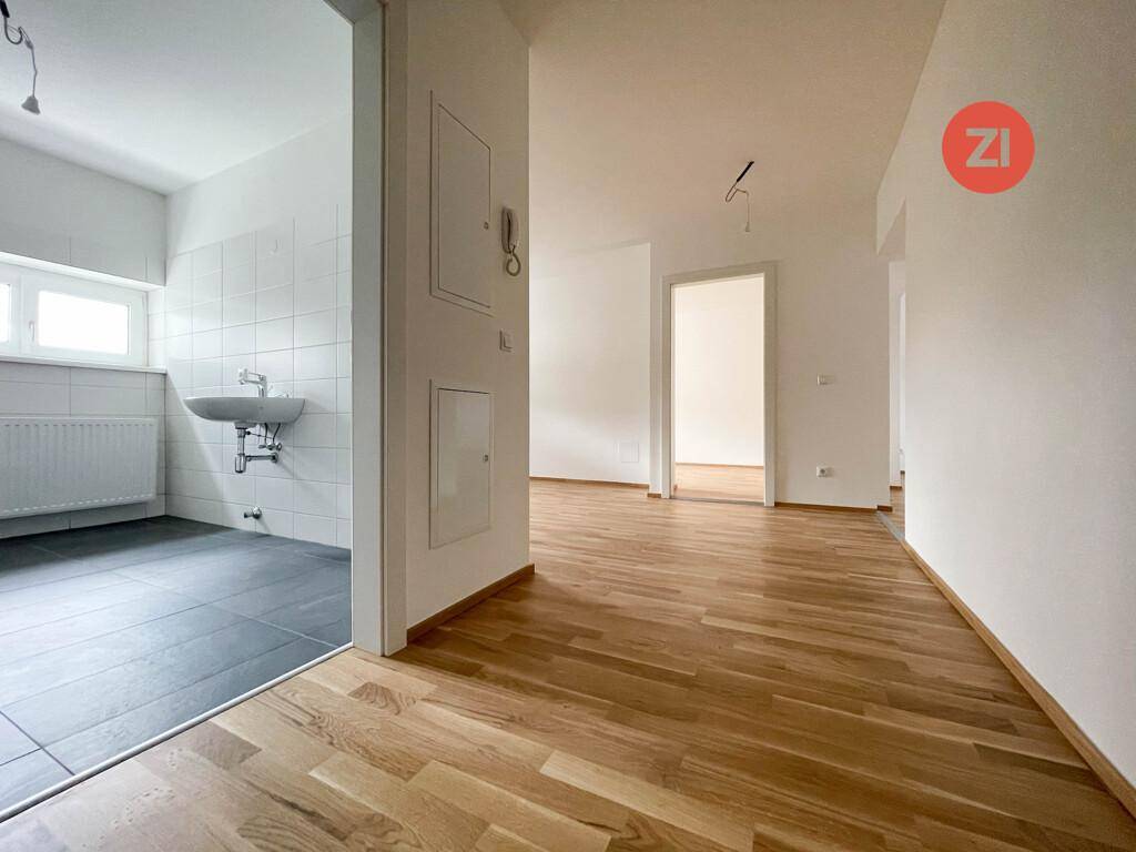 Heller Flur mit Parkettboden, der zu weiteren Zimmern führt, mit Blick in ein gefliestes Bad.