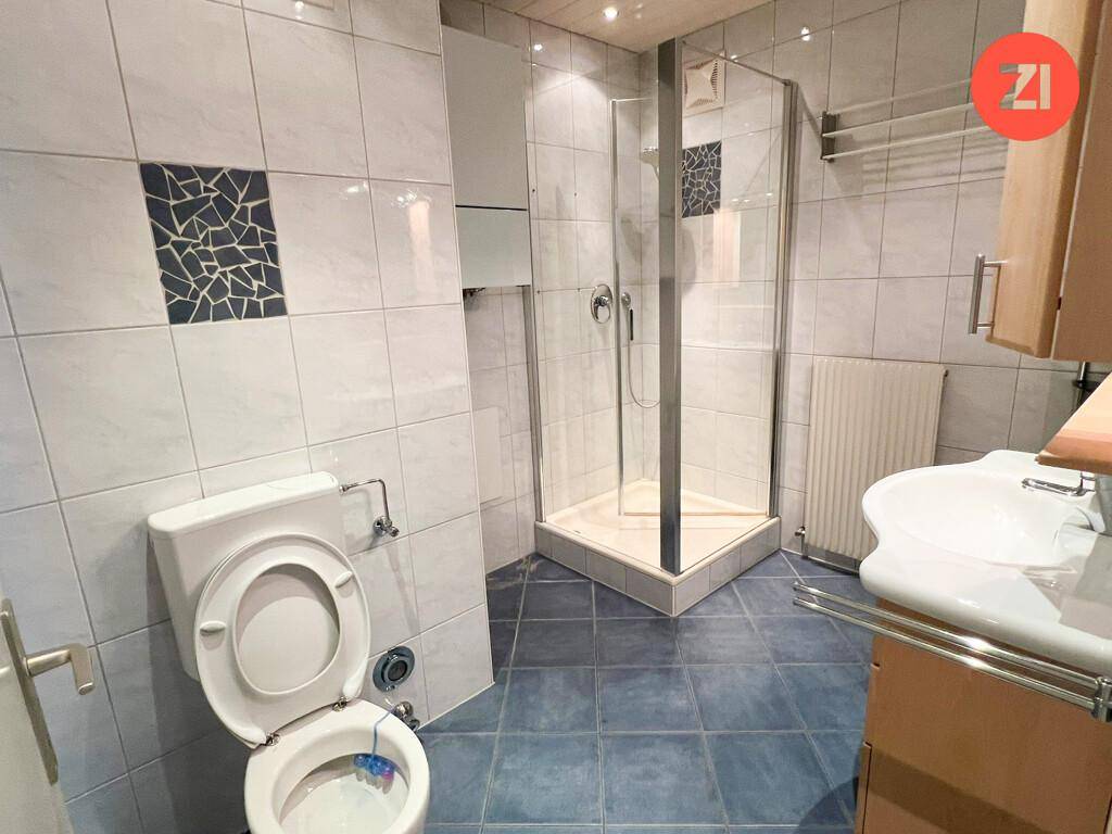 Badezimmer mit Dusche, WC, Waschbecken und blauen Fliesenakzenten.