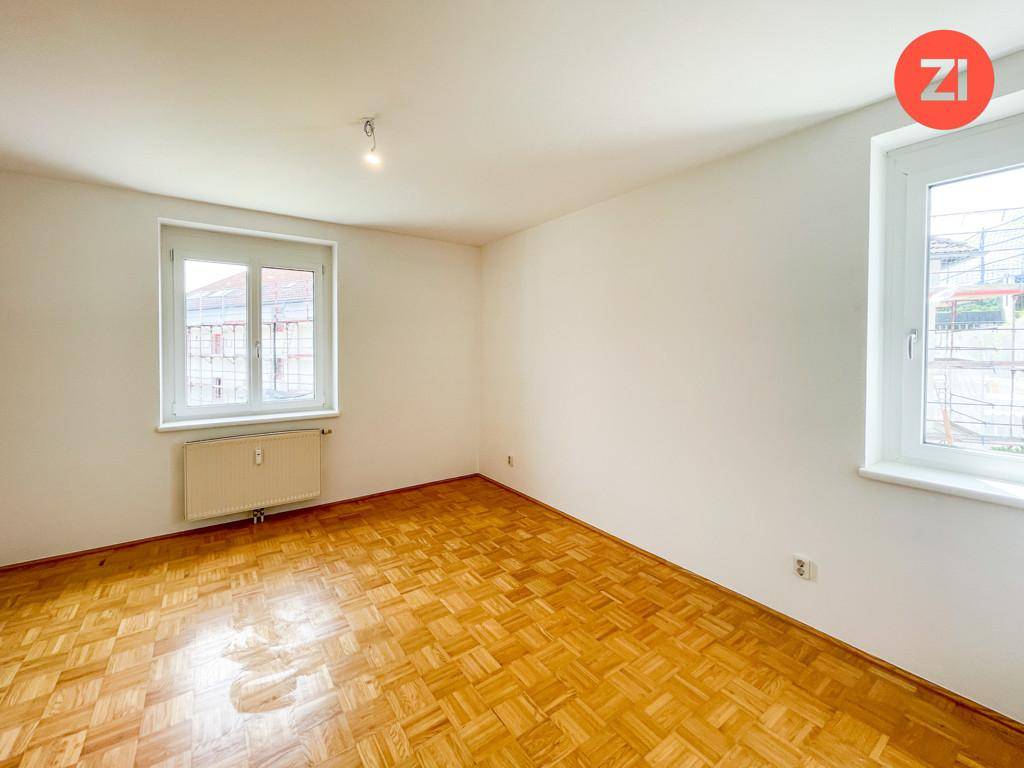 Schlafzimmer mit Parkettboden und zwei Fenstern, die viel Tageslicht hereinlassen.