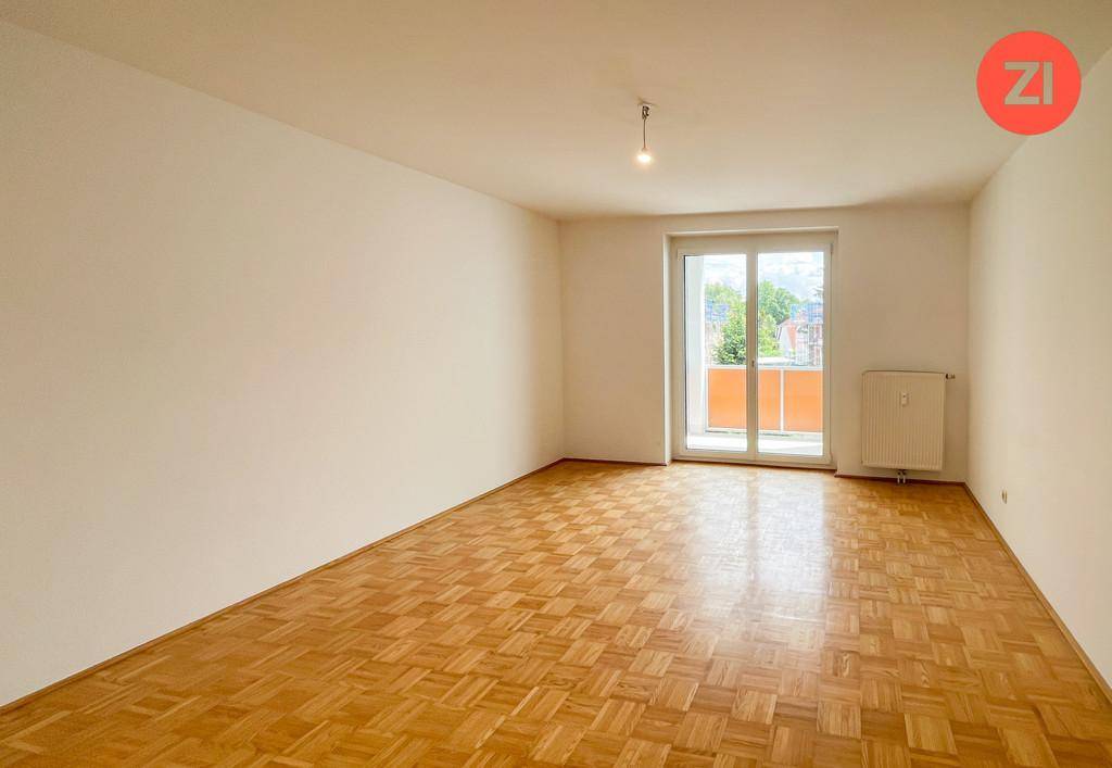 Helles Wohnzimmer mit Parkettboden, großem Fenster und Zugang zu einem Balkon.