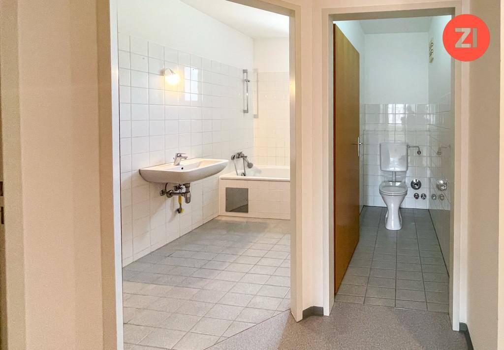 Flur mit Blick in das Badezimmer und eine separate Toilette, beide mit Fliesenboden.