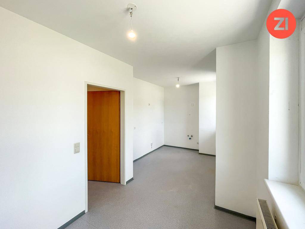 Heller, leerer Raum mit grauem Boden und einem Fenster, das Tageslicht spendet.