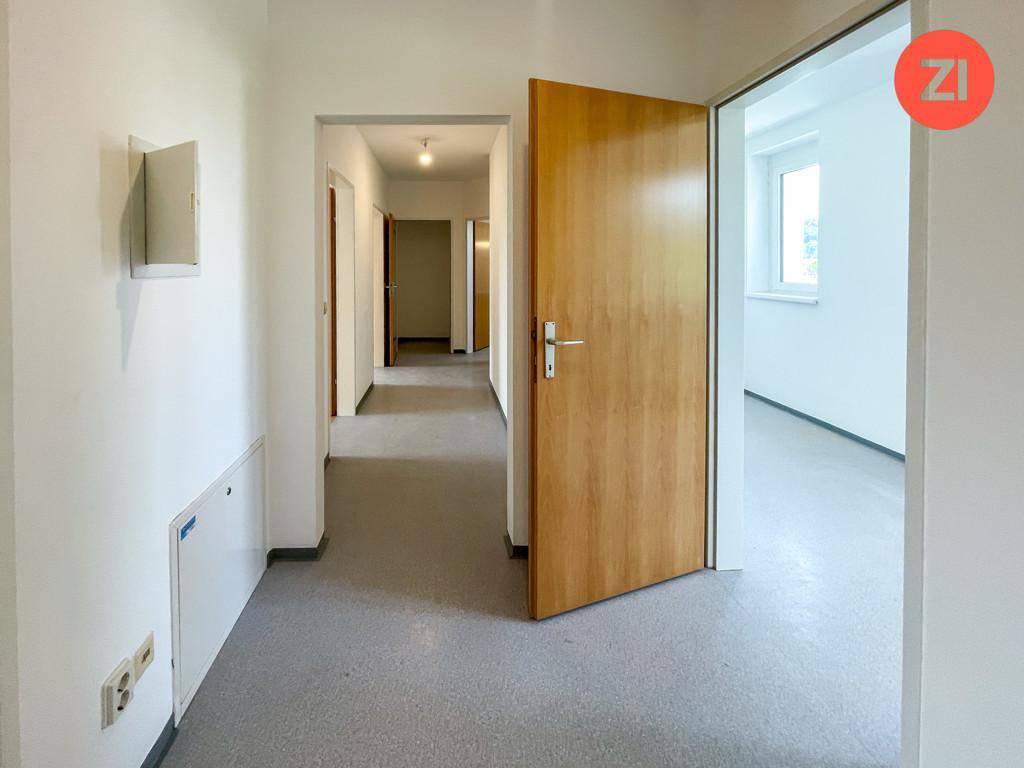 Heller Flur mit grauem Boden und Holztüren, der zu verschiedenen Räumen führt.