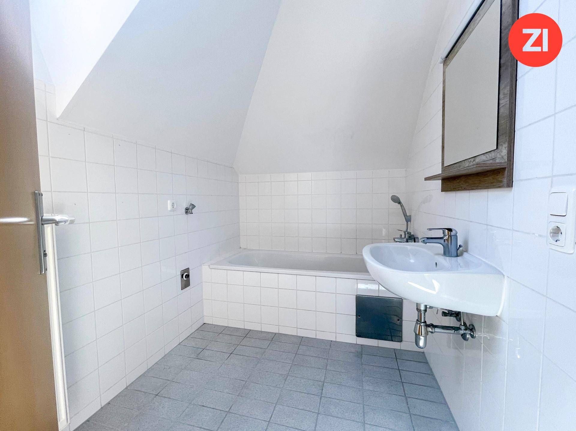 Badezimmer mit weißen Fliesen, Badewanne und Waschbecken unter der Dachschräge.
