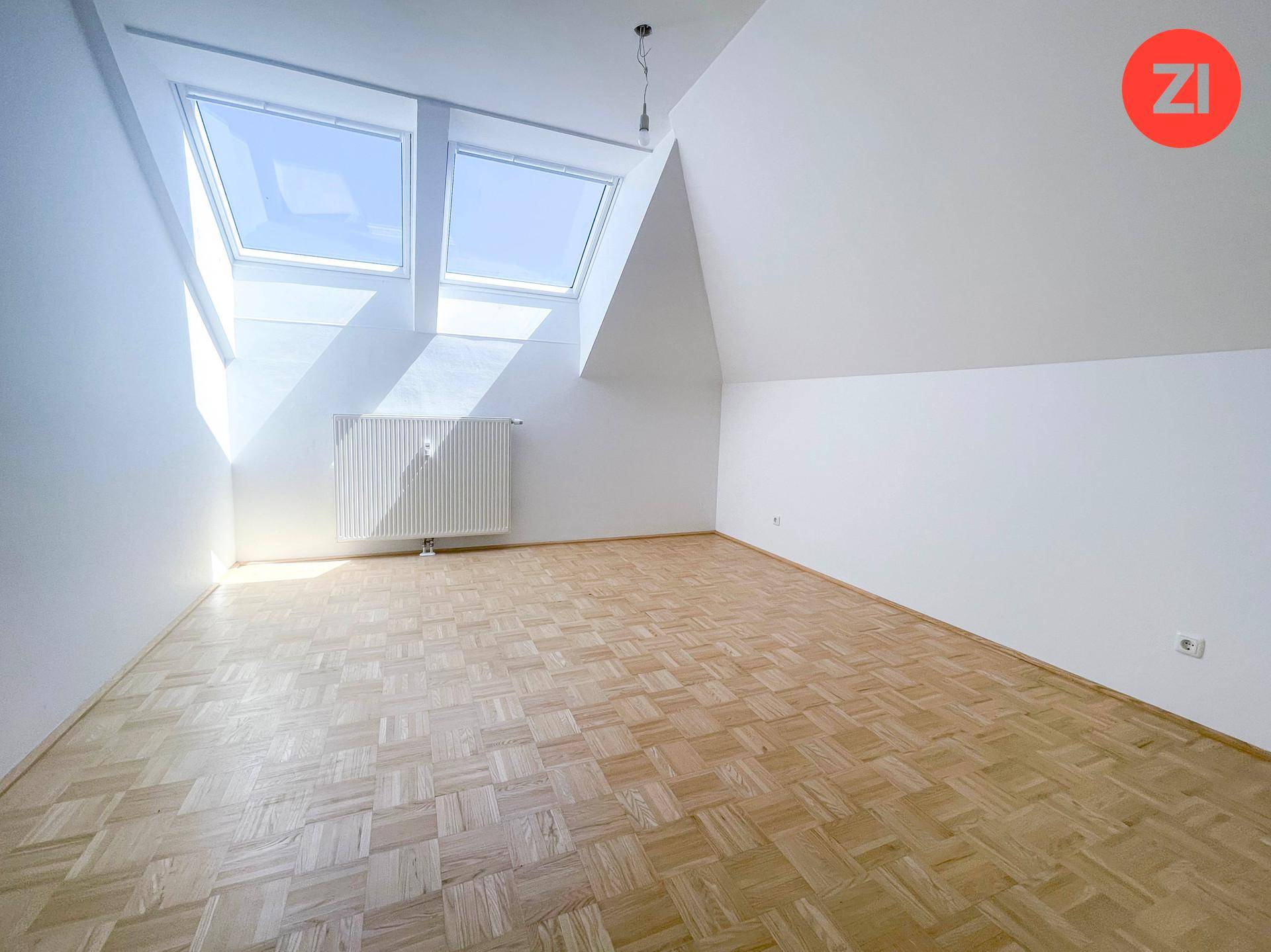Heller Raum mit Parkettboden, Dachschrägen und zwei großen Dachfenstern.