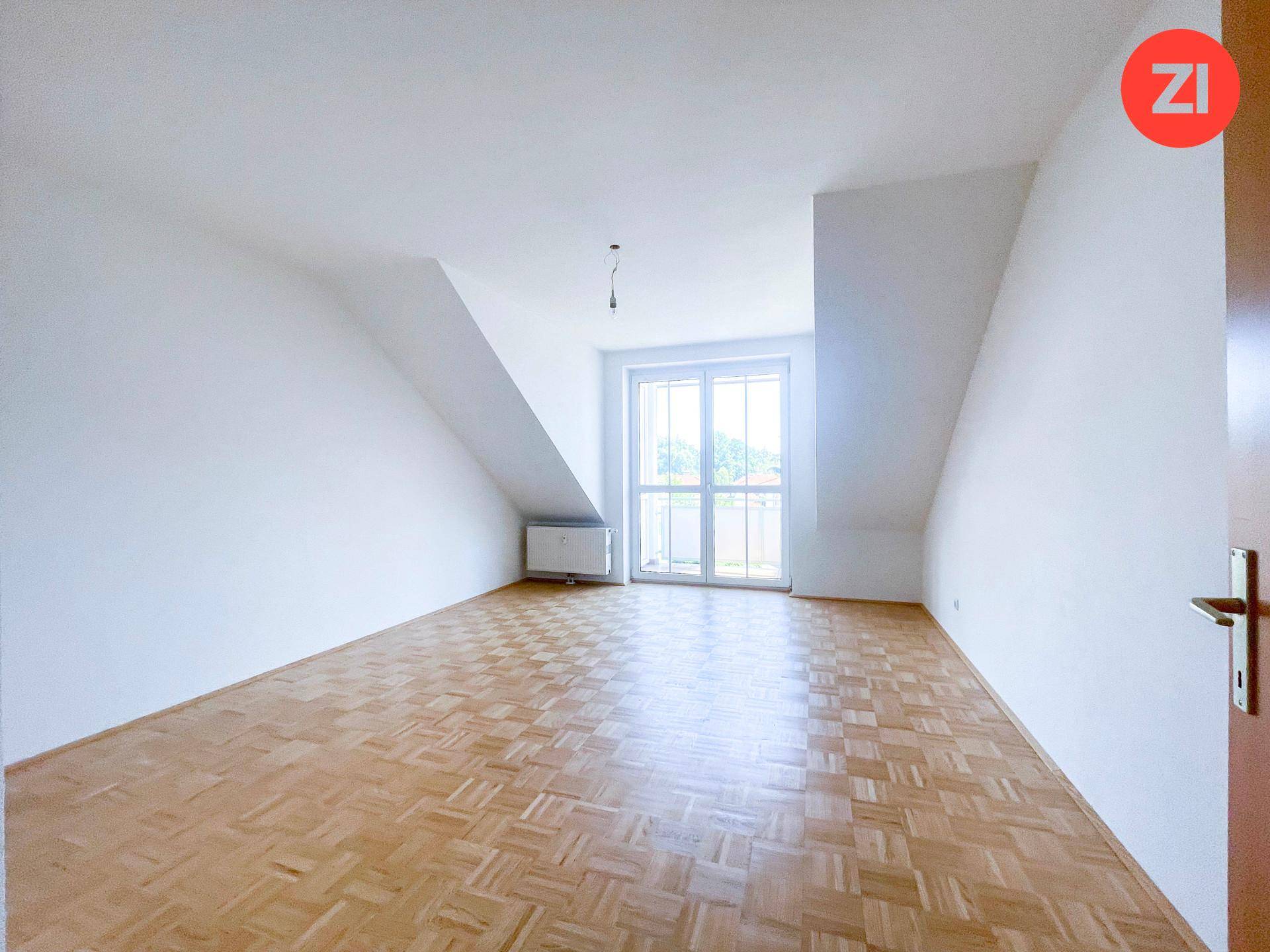 Heller Raum mit Parkettboden, Dachschrägen und großem Fenster mit Ausblick.