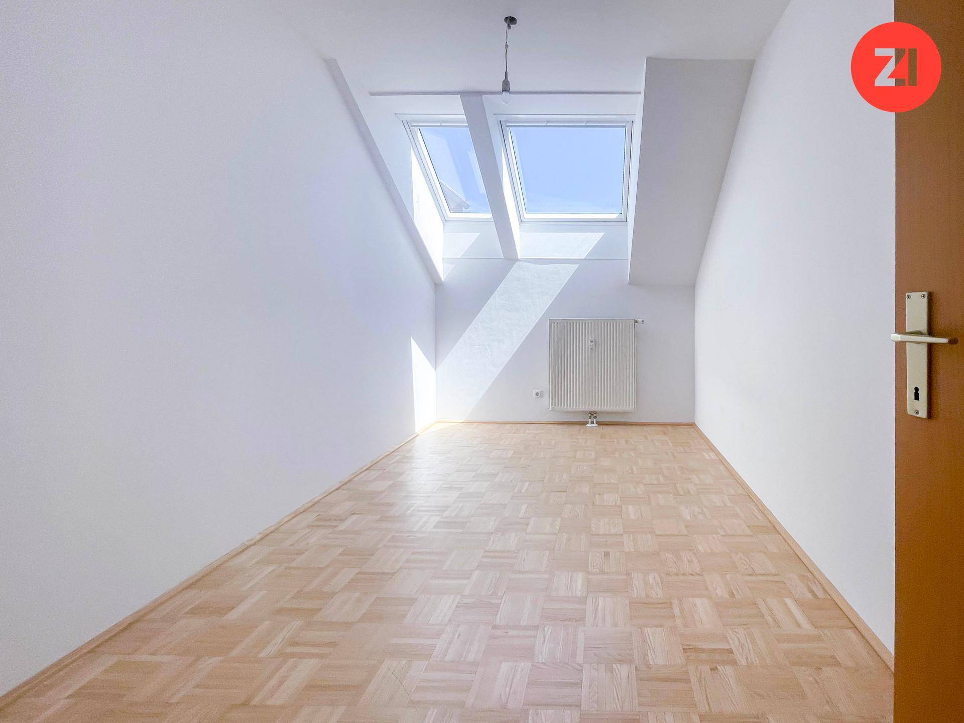 Lichtdurchfluteter Raum mit Parkettboden, Dachschrägen und zwei großen Dachfenstern.