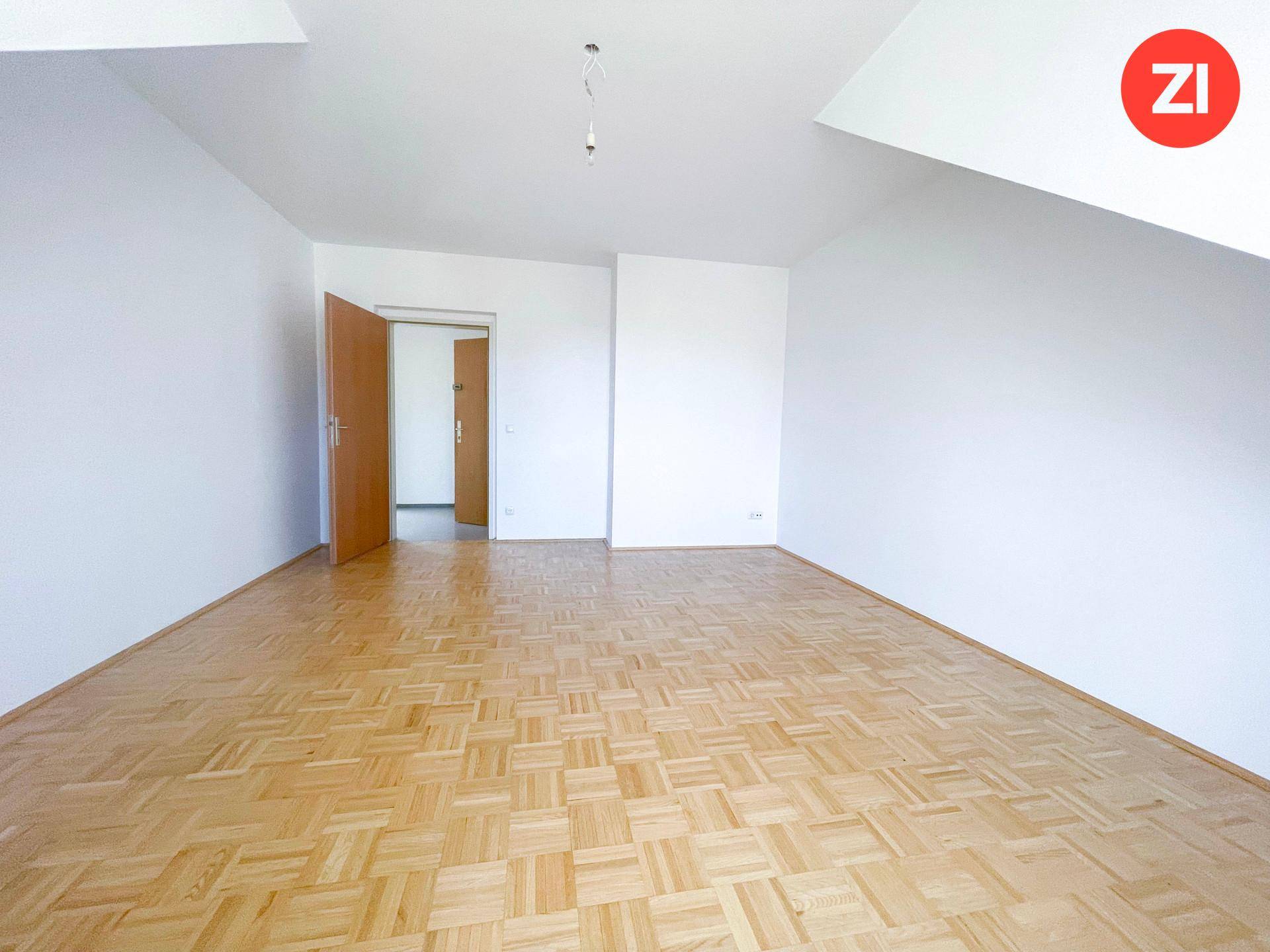 Leerer Raum mit Parkettboden, weißen Wänden und Zugang zu einem weiteren Zimmer.