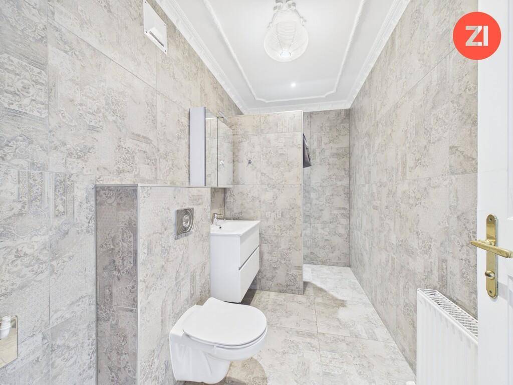 Modern gefliestes Badezimmer mit wandhängendem WC, Waschbecken und Spiegelschrank.