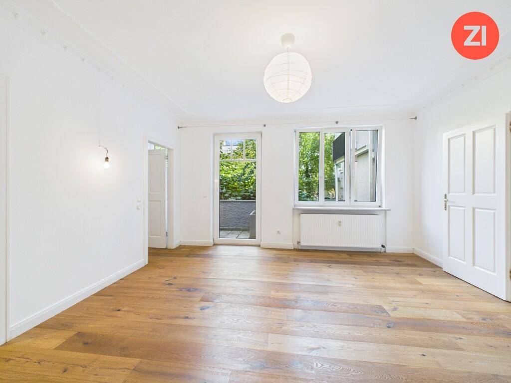 Geräumiges Wohnzimmer mit großen Fenstern, Holzboden und klassischer Stuckverzierung an der Decke.