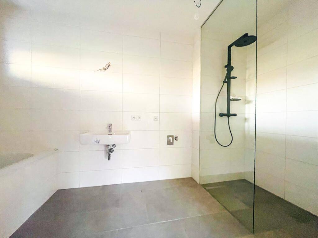 Modernes Badezimmer mit weißen Fliesen, ebenerdiger Dusche und minimalistischem Waschbecken.