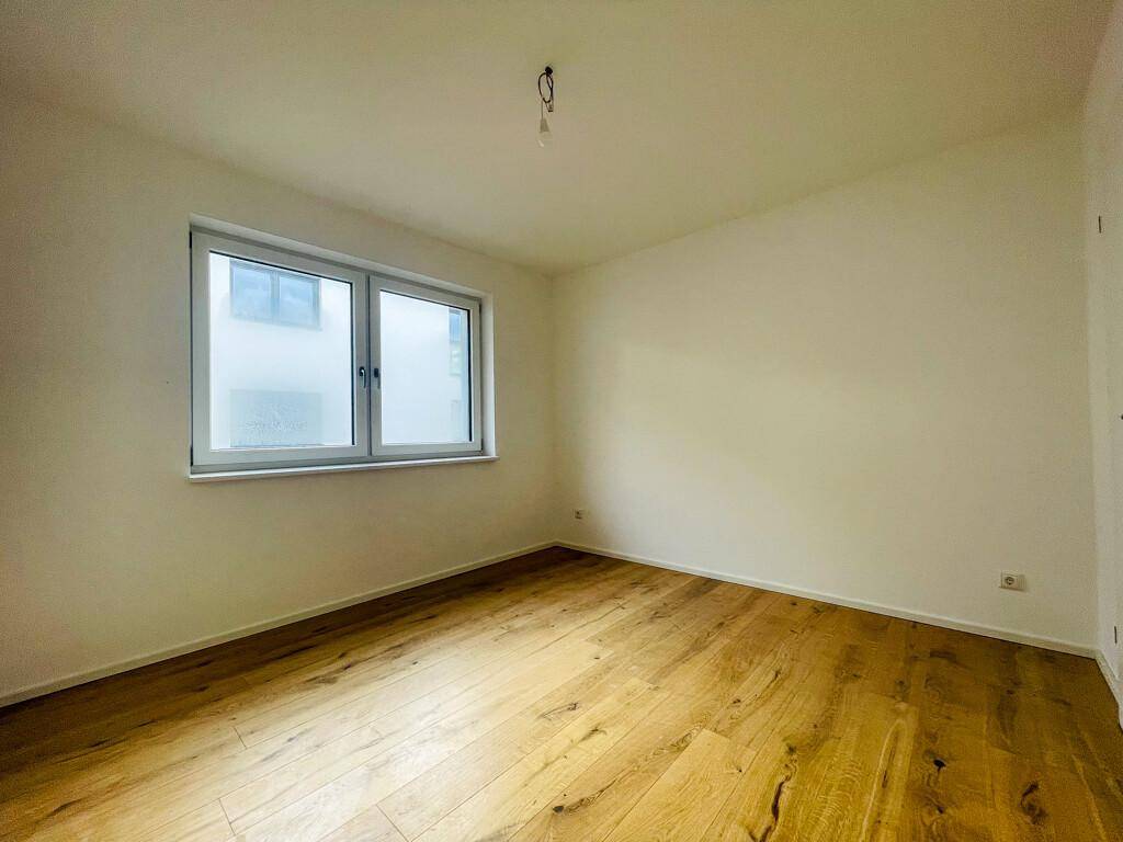 Leeres Schlafzimmer mit hellem Holzparkettboden und einem Fenster, das für ausreichend Tageslicht sorgt.