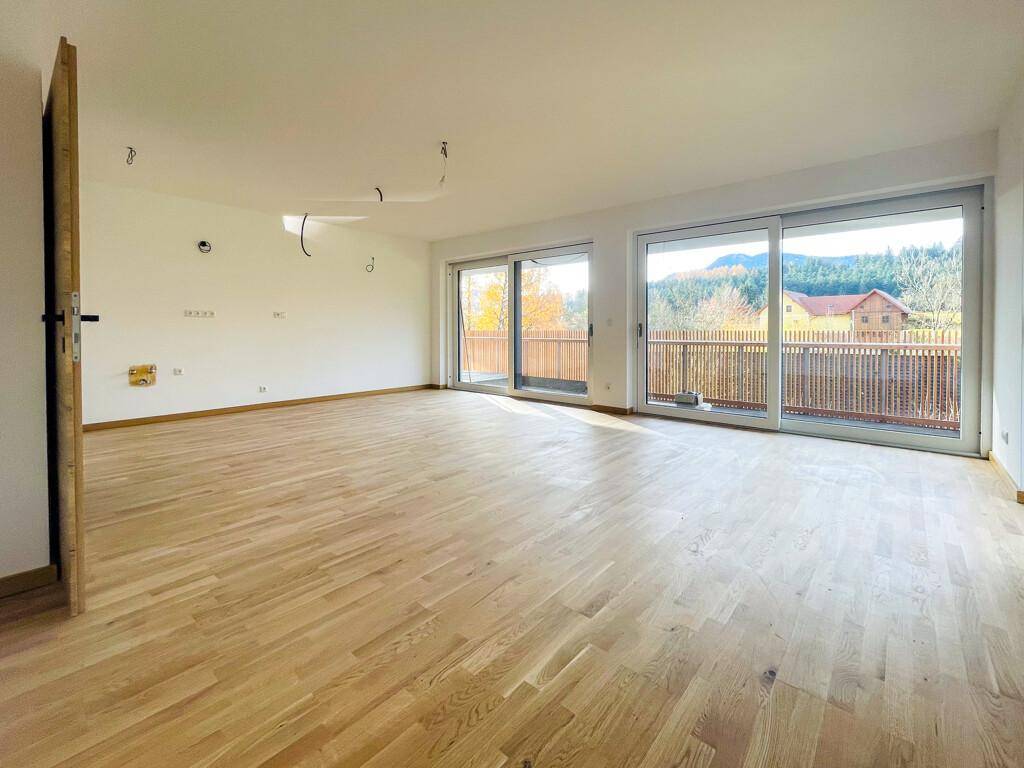 Geräumiges Wohnzimmer mit hellem Holzparkett und Zugang zu einem Balkon mit schöner Aussicht.