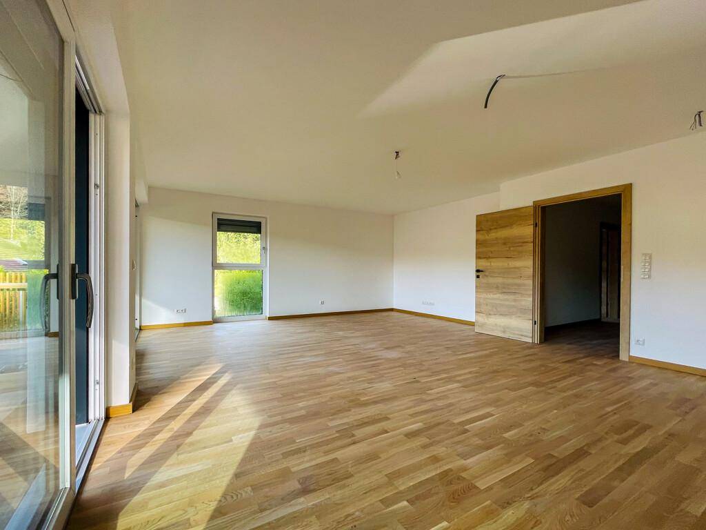 Heller Wohnbereich mit Holzparkettboden, großen Fenstern und einer modernen Holztür.