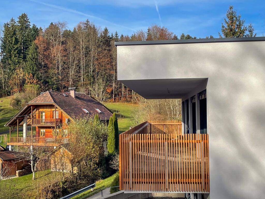 Moderner Balkon mit Holzgeländer und Blick auf ein traditionelles Holzhaus in grüner Umgebung.