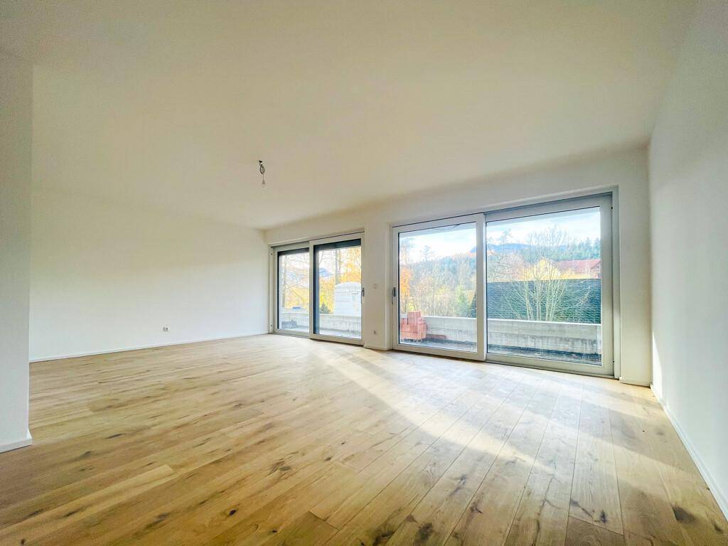 Helles, leeres Wohnzimmer mit neuem Holzparkettboden und großen Schiebetüren, die viel Tageslicht hereinlassen.