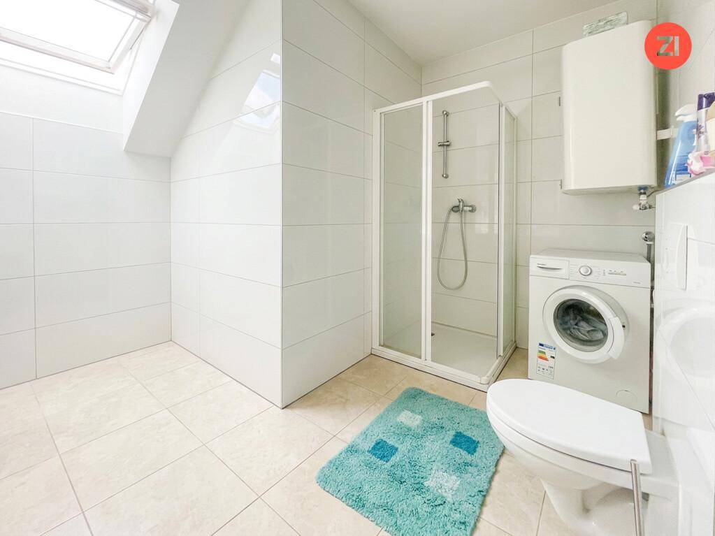 Gefliestes Badezimmer mit Duschkabine, Toilette, Waschmaschine und Dachfenster.