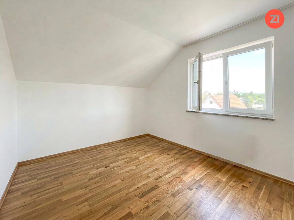 Leeres Schlafzimmer mit Holzboden, Dachschräge und einem Fenster mit Ausblick.