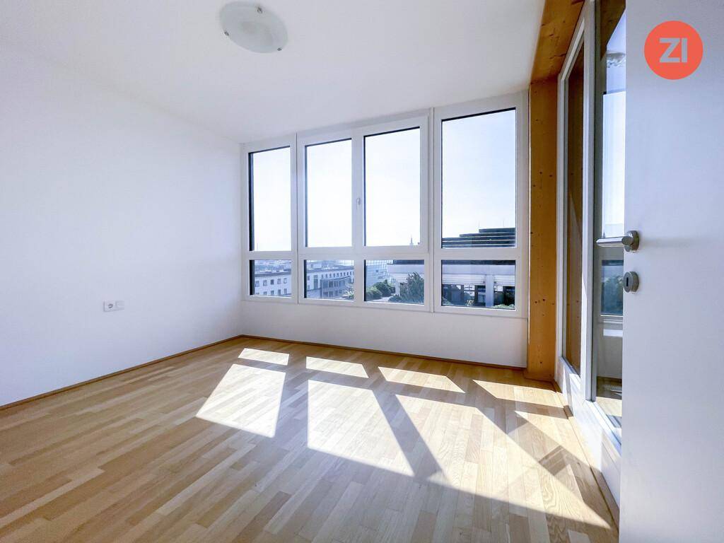 Geräumiges Zimmer mit viel Tageslicht durch große Fenster und hellem Parkettboden.