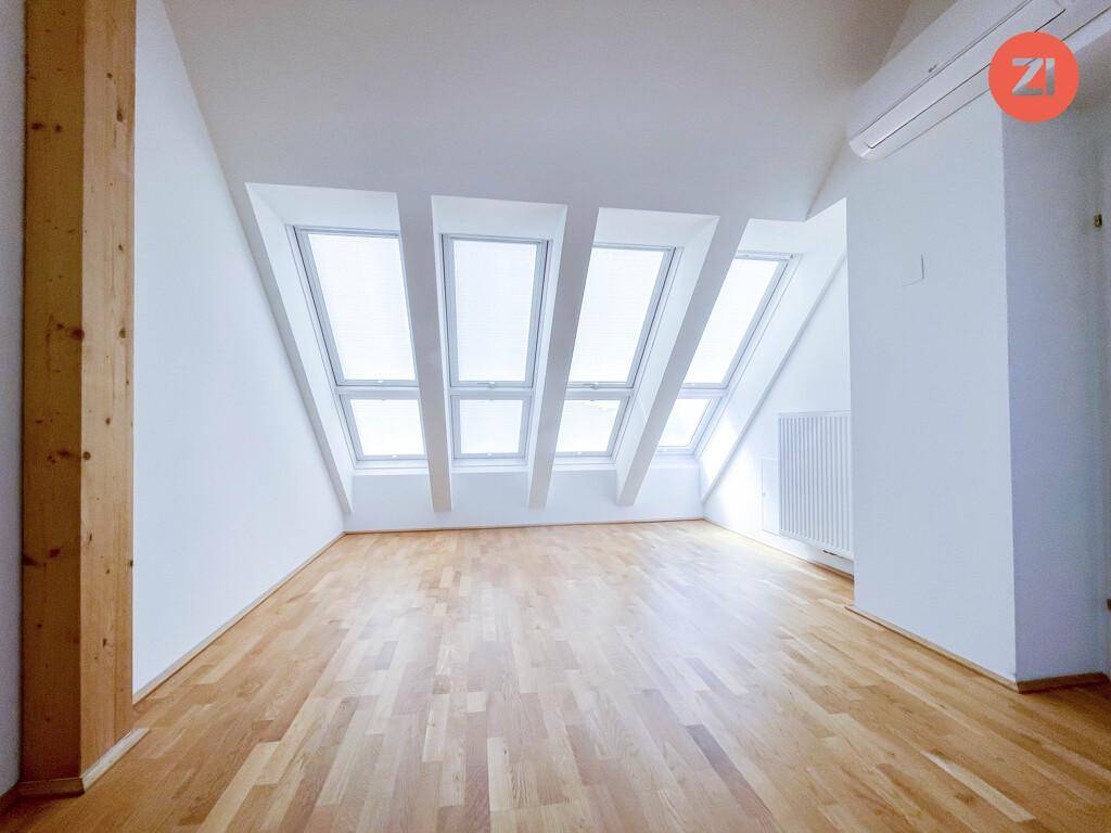 Geräumiges Dachzimmer mit mehreren Dachfenstern, die viel Tageslicht hereinlassen, und Holzboden.