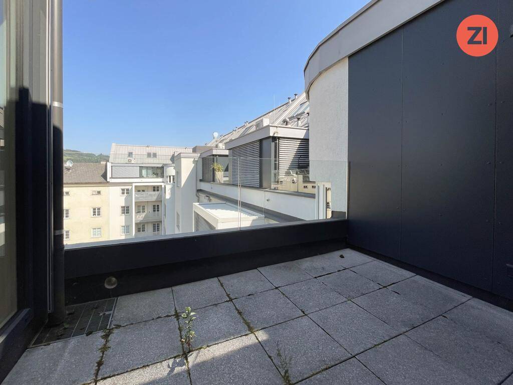 Dachterrasse mit grauen Fliesen und Blick auf die umliegenden Gebäude und die Stadt.