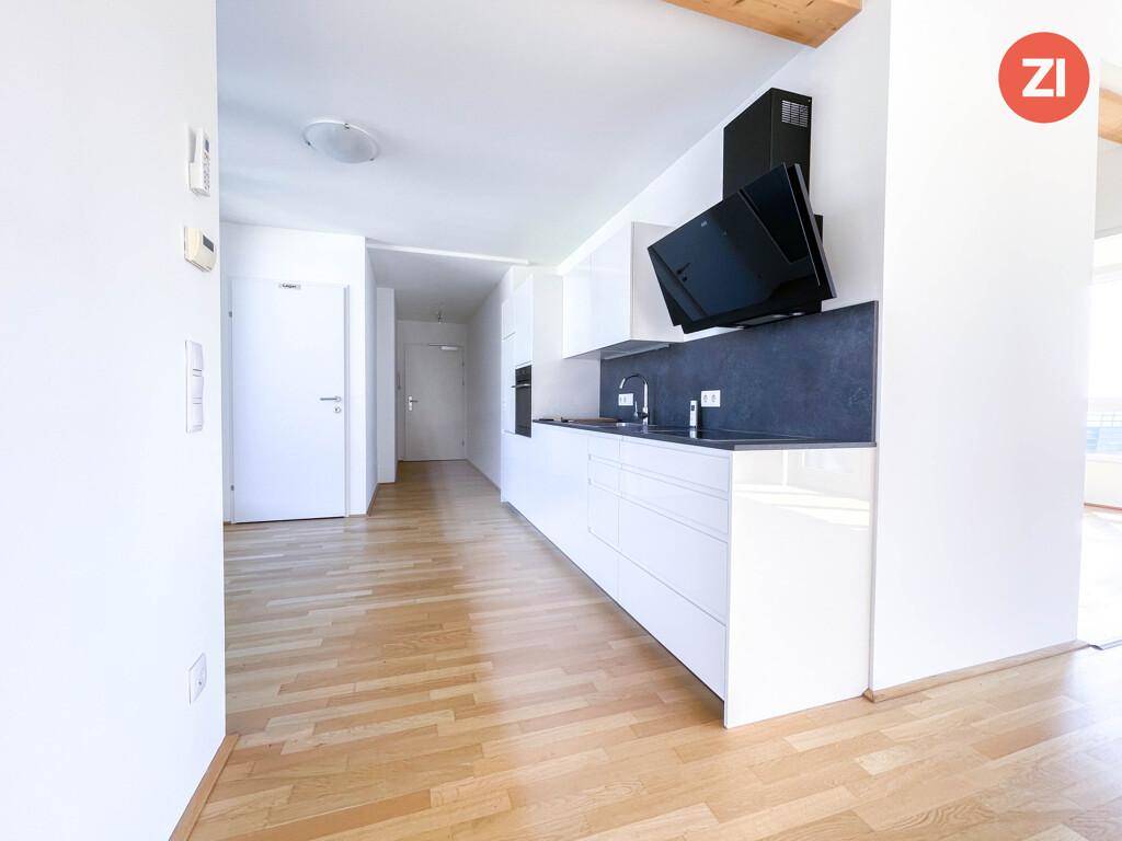 Moderne, offene Küche mit weißen Hochglanzfronten, dunkler Arbeitsplatte und integrierten Geräten.