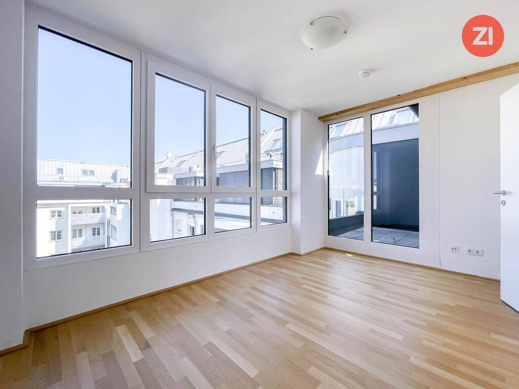 Helles Zimmer mit großen Fenstern, Holzboden und Zugang zu einem Außenbereich.