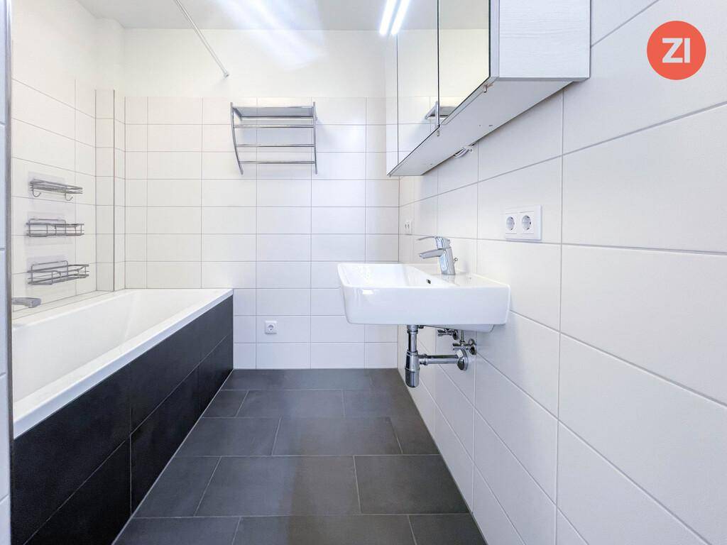 Modernes Badezimmer mit weißen Wandfliesen, dunklem Boden und Badewanne.