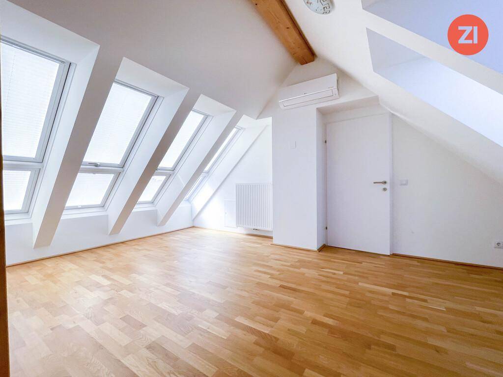 Heller Dachraum mit schrägen Wänden, mehreren Dachfenstern und Zugang zu weiteren Räumen.