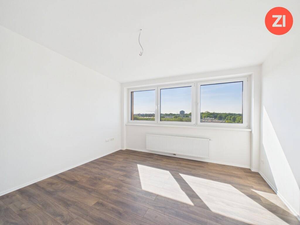 Lichtdurchflutetes Zimmer mit Laminatboden und Heizkörper unter den großen Fenstern.