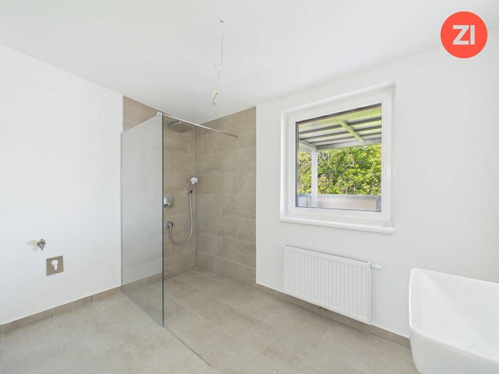 Geräumiges Badezimmer mit ebenerdiger Dusche, Fenster und Platz für weitere Ausstattung.
